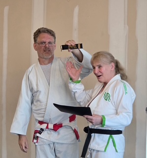 David J. Ellis presenting Manon Saulnier with her Nidan rank certificate and a black belt key chain on July 2, 2026
